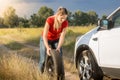 Young woman rolling spare wheel to change flate tyre on her car