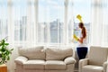 Woman in rubber gloves cleaning window with cleanser spray and yellow rag at home, copy space, back view. People, housework.