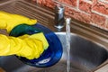 Woman in rubber yellow gloves wash dishes and plates with sponge in the metal sink at the kitchen. Royalty Free Stock Photo