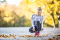 Woman runner tying shoelaces before jogging in autumn tree alley park. Sports female autumn outfit leggings and thermal underwear