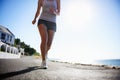 Woman, running and asphalt at beach for fitness, workout or outdoor cardio training on a sunny day. Closeup of athlete