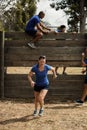 Woman running while trainer assisting men to climb a wooden wall Royalty Free Stock Photo