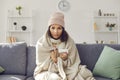 Woman with a runny nose sits in front of the webcam on the couch wrapped in a plaid and hat Royalty Free Stock Photo