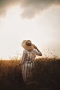 Woman in rustic dress and hat enjoying peaceful sunset in wildflowers and herbs in summer meadow. Atmospheric authentic moment. Royalty Free Stock Photo