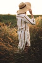 Woman in rustic dress and hat enjoying peaceful sunset in wildflowers and herbs in summer meadow. Atmospheric authentic moment. Royalty Free Stock Photo