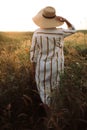 Woman in rustic dress and hat enjoying peaceful sunset in wildflowers and herbs in summer meadow. Atmospheric authentic moment. Royalty Free Stock Photo