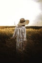 Woman in rustic dress and hat enjoying peaceful sunset in wildflowers and herbs in summer meadow. Atmospheric authentic moment. Royalty Free Stock Photo