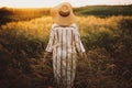 Woman in rustic dress and hat walking in wildflowers and herbs in sunset golden light in summer meadow. Atmospheric authentic Royalty Free Stock Photo