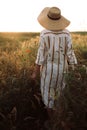 Woman in rustic dress and hat walking in wildflowers and herbs in sunset golden light in summer meadow. Atmospheric authentic Royalty Free Stock Photo
