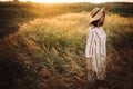 Woman in rustic dress and hat walking in wildflowers and herbs in sunset golden light in summer meadow. Stylish girl enjoying Royalty Free Stock Photo