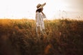 Woman in rustic dress and hat walking in wildflowers and herbs in sunset golden light in summer meadow. Stylish girl enjoying Royalty Free Stock Photo