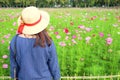 Woman`s back wearing straw hat while looking at flower garden.