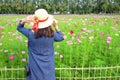 Woman`s back wearing straw hat while looking at flower garden.