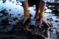 A woman's bare feet and hands with luxury bracelets and rings in a dirty puddle of black mud Royalty Free Stock Photo