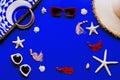 Woman`s beach accessories: bag, straw hat, sunglasses, earrings, starfish and shells on electric blue background Royalty Free Stock Photo