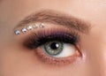 Woman`s blue green eye with beautiful make-up and thick eyebrows, crystals under the eyebrow  close up.  Looking at the camera. Royalty Free Stock Photo