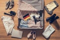 Woman`s clothes, laptop, camer and flag of Germany lying on the parquet floor near and in the open suitcase. Travel concept.