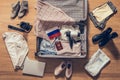 Woman`s clothes, laptop, camera, russian pasport and flag lying on the parquet floor near and in the open suitcase. Travel concep