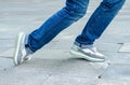 woman's feet in jeans and sneakers tripping over unevenly laid paving slabs. Accident injury on walk