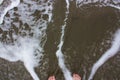 A woman`s feet with red toenails in the foamy, shallow water of the Pacific Ocean on a sandy beach in Hawaii