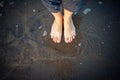 Woman`s feet on sandy beach, standing in ocean water, copy space. Pedicured feet with red nail polish on toes in the sea. Bare Royalty Free Stock Photo