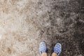 Woman`s feet in walking shoes on asphalt road. Industrial concrete floor top view photo.