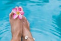 Woman`s female legs in blue swimming pool water with frangipani Royalty Free Stock Photo