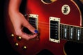A woman`s fingers with a manicure lies on the strings of a red guitar. Girl guitarist playing in the recording Studio Royalty Free Stock Photo