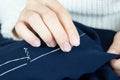 Woman`s fingers with thread and needle stitching fabric. Hands sewing, repairing clothes Tailoring and homecraft concept