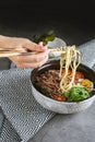 a woman`s hand with a beautiful manicure holds wooden sticks with noodles. there is a napkin on the gray table and a plate Royalty Free Stock Photo
