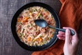 WomanÃ¢â¬â¢s hand with black metal spoon, Puerto Rican Chicken Rice Soup in a black stoneware bowl on a dark wood table, orange cloth