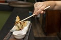 Woman\'s hand with chopsticks dipping a gyoza in soy sauce and then gobbling it up with delight