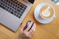 Woman`s hand clicking on wireless mouse with laptop and cup of coffee besides on wooden table.Top view. Royalty Free Stock Photo