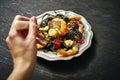 A woman`s hand and delicious black spaghetti with grilled shrimps and vegetables, on silver plate Royalty Free Stock Photo