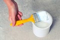 A woman`s hand dips a yellow brush into a jar of white paint. Painting of walls and other surfaces during repair with white ename