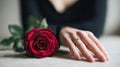 Woman\'s hand with elegant engagement ring resting on table next to a single red rose symbolizing romance and commitment in Royalty Free Stock Photo