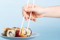 A woman hand with a French manicure lifts sushi rolls white sticks. Blue background soft light close-up Royalty Free Stock Photo