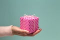 Woman`s hand giving pink gift box in polka dots