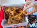 Woman`s hand grabbing piece of Popeyes Louisiana Chicken from dinner box in restaurant