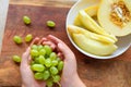 A woman`s hand with green grapes, plate of melon slices on a wooden background, concept of fresh sweet fruits and healthy food Royalty Free Stock Photo