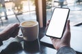 A woman`s hand holding black mobile phone with blank white desktop screen with laptop and coffee cup on table in caf Royalty Free Stock Photo