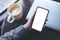 A woman`s hand holding black mobile phone with blank white desktop screen with laptop and coffee cup on table in cafe Royalty Free Stock Photo