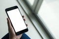 Woman`s hand holding black mobile phone with blank white screen on thigh with white tile floor and sliding door background Royalty Free Stock Photo