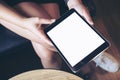 Woman`s hand holding black tablet with blank white screen on thigh with wooden floor background in modern cafe Royalty Free Stock Photo