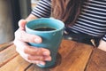 A woman`s hand holding blue mug of hot coffee on vintage wooden table in cafe Royalty Free Stock Photo