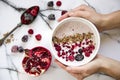 Woman`s hand holding a bowl of yoghurt with cereals and forest fruits. Pomegranate on the table besides. Royalty Free Stock Photo