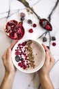 Woman`s hand holding a bowl of yoghurt with cereals and forest fruits. Pomegranate on the table besides. Royalty Free Stock Photo