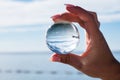 Woman hand holding a crystal ball, looking through to the ocean and sky. Creative photography