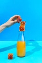 Woman`s hand holding cube made of red oranges onto the glass bottle with citrus juice