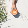 Woman`s hand holding cup of coffee or tea on a white background. Drawing a heart in a mug. Top view. Outdoor.Take away.